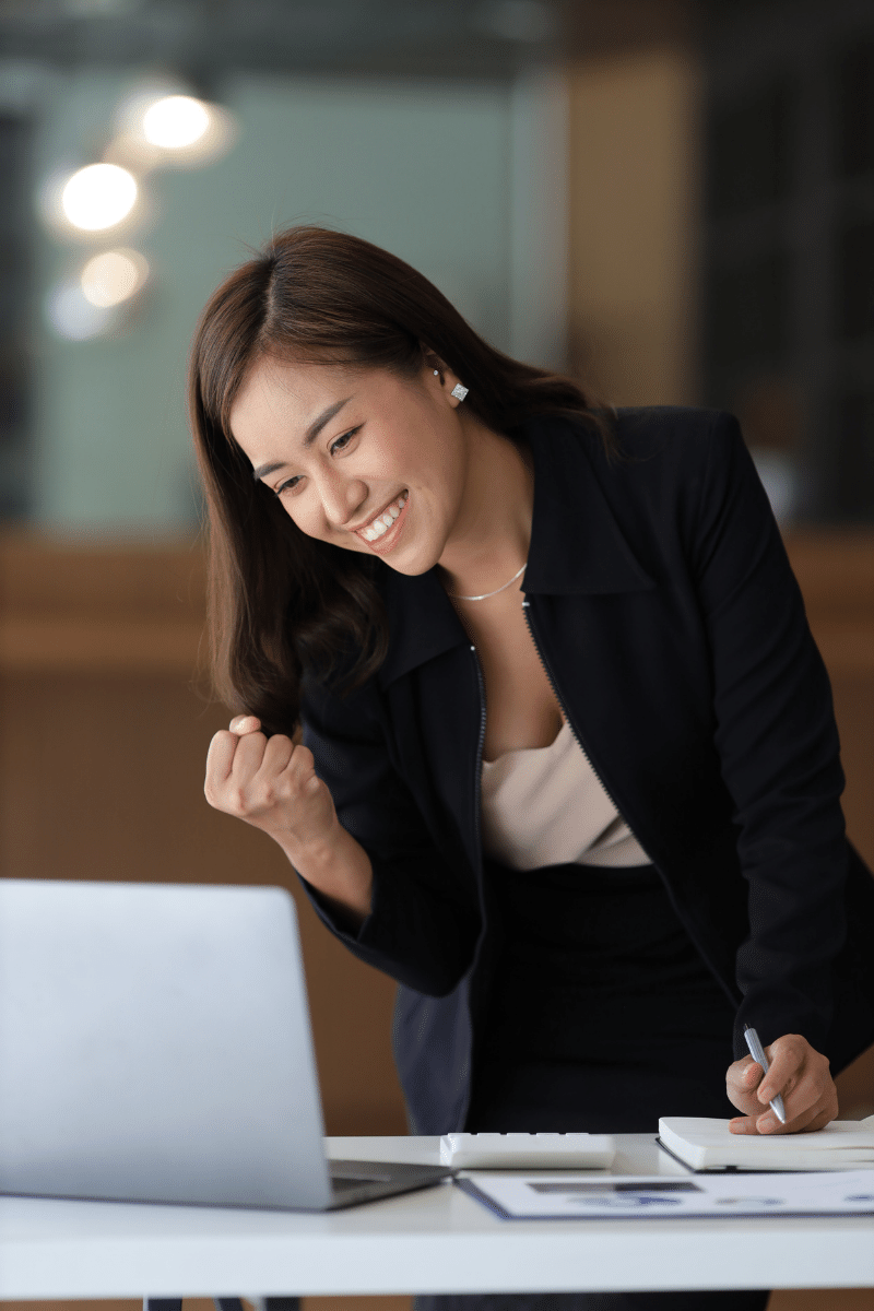 A business woman or secretary working on a laptop expresses her joy while looking at the laptop screen. Asian female emplo