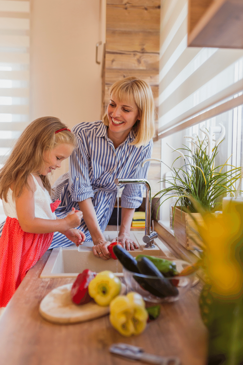 Beautiful happy mother and daughter having fun washing vegetables for salad in the kitchen