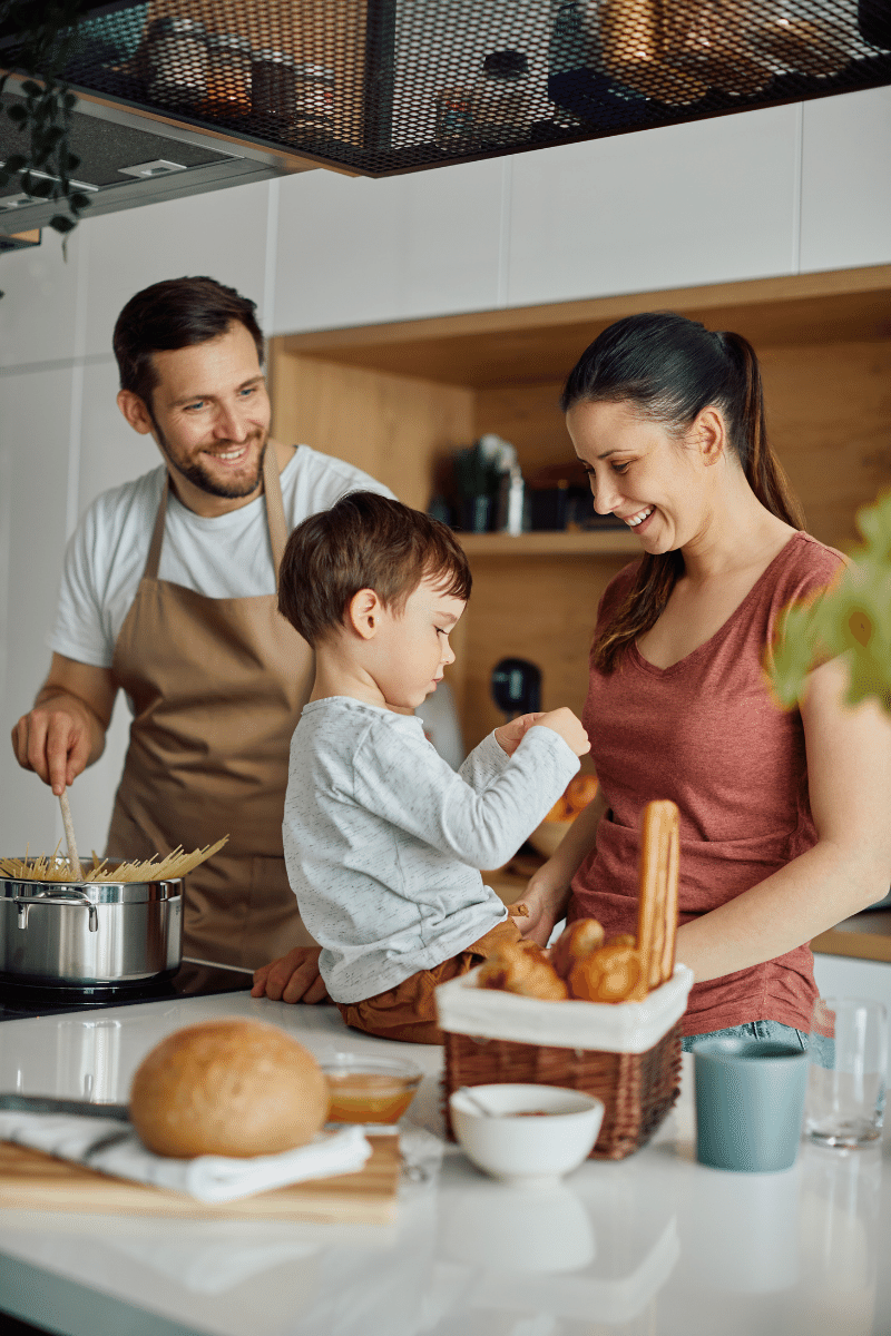 Happy parents having fun while preparing food with their small son in the kitchen