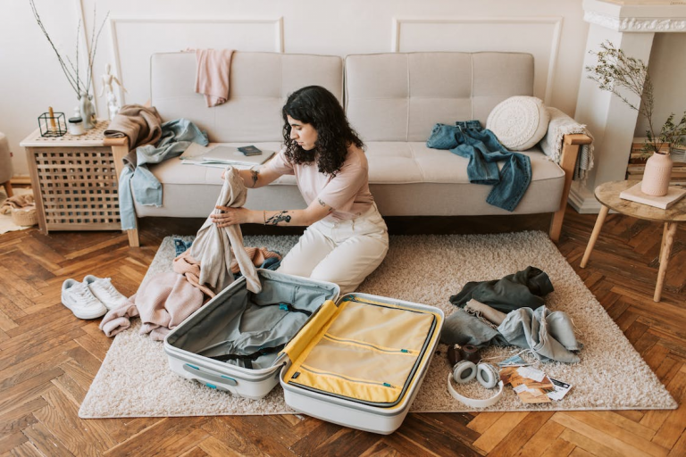 A Woman Packing her Holiday Luggage in a Living Room with Clothes Strewn all Over the Couch and Rug